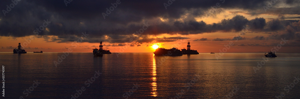Panoramic from the coast at sunrise with ships in the bay, cloudy sky and calm sea