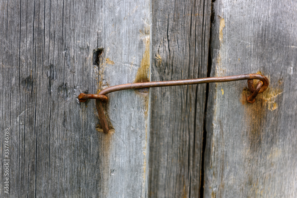Close-up of weathered, unpainted wooden door, locked on metal hinge. Vintage background from pine shabby plank with rusty lock.