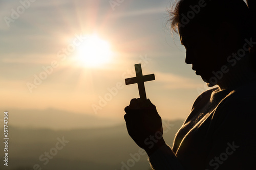 human hands praying to the GOD while holding a crucifix symbol with bright sunbeam.