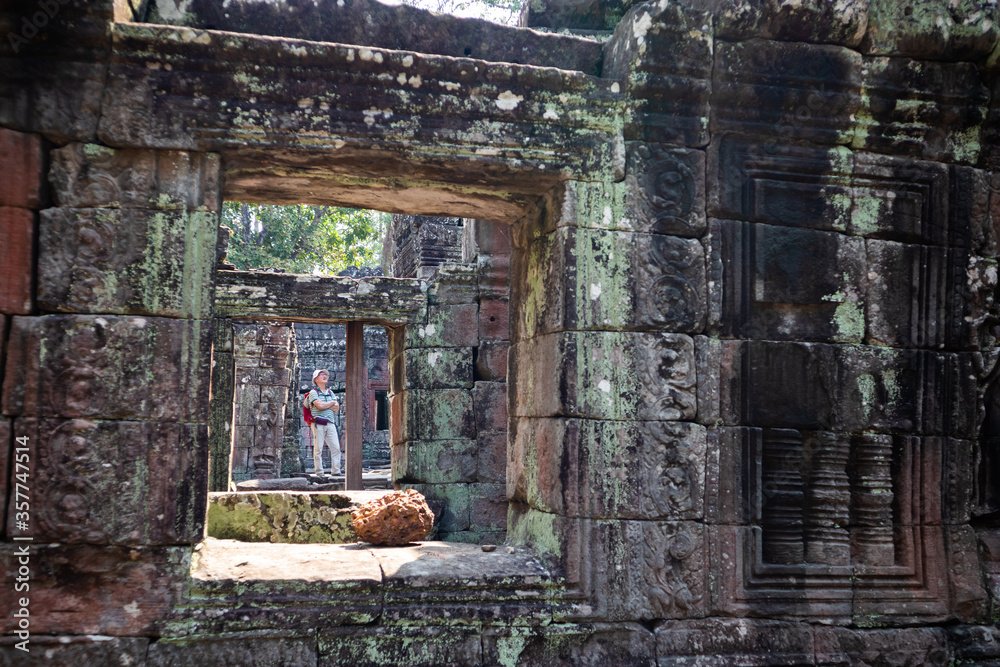 Man tourist visiting the ruins of Banteay Kdei temple. He wears a hat and a red backpack. Pictured through the windows. Asian tourist. Angkor area, Siem Reap, Cambodia, South east Asia