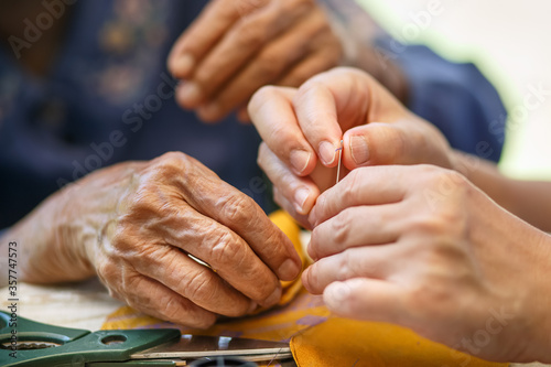 Caregiver holding thread the needle for elderly woman in the cloth crafts occupational therapy for Alzheimers or dementia photo