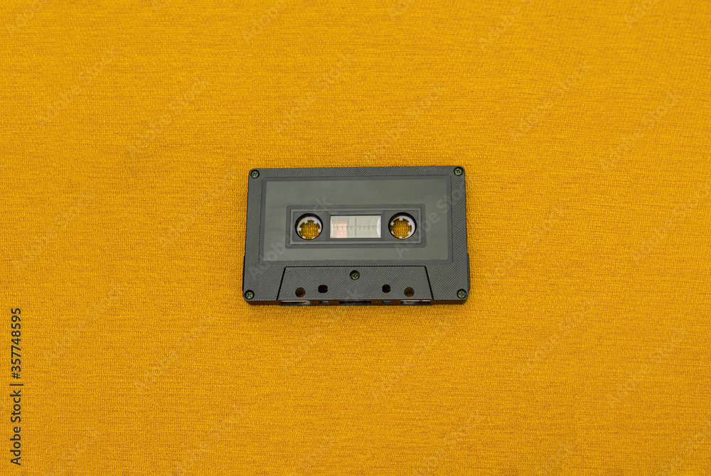 Obraz premium Top View of an old black cassette over a yellow cloth. Fashion and retro music concept