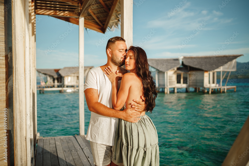 Couple looking each other in love on vacations with the sea in the background. Romantic young couple stand on a jetty anear water bungalow by the sea