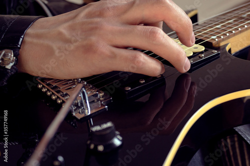 Bottom view of a young male using a leather jacket playing a black and yellow electric guitar at indoor. Rock and music concept © Alejandro Bernal