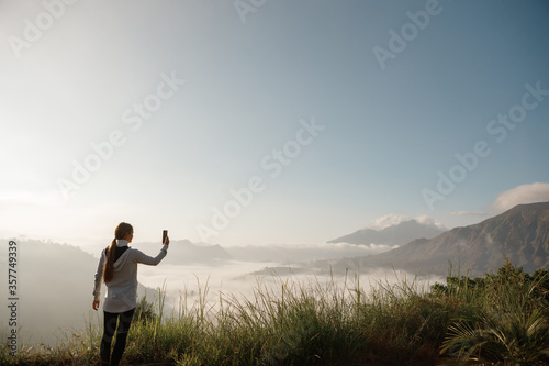 Young cucasian woman backpacker taking photo with smartphone on mountain peak. Nice young woman using her mobile phone while enjoying her weekend in the mountains