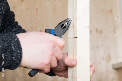 close-up, pliers, pulls a metal nail out of a wooden bar photo