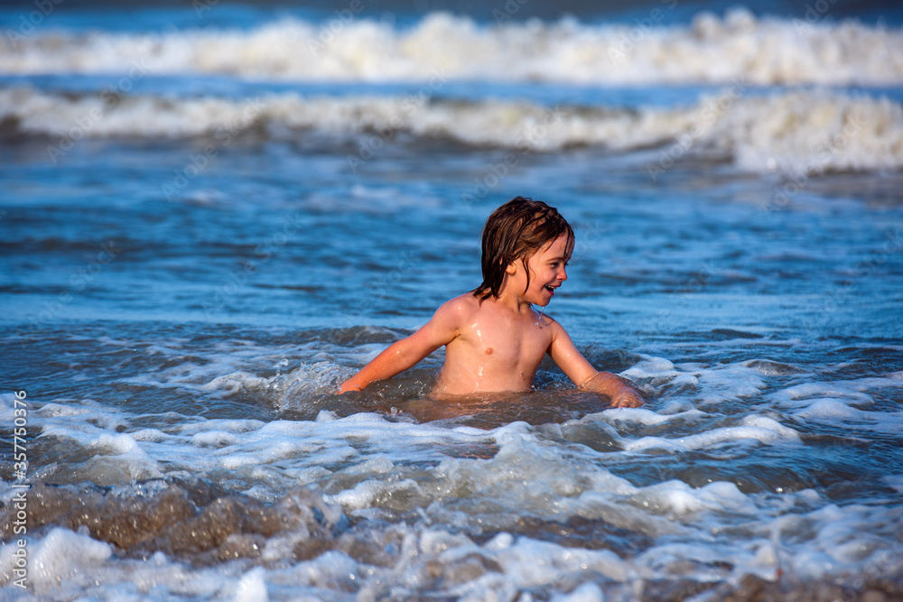 Happy boy enjoys life on summer beach. Cute kid having fun on sandy beach in summer. Ocean or sea wawes on the background.