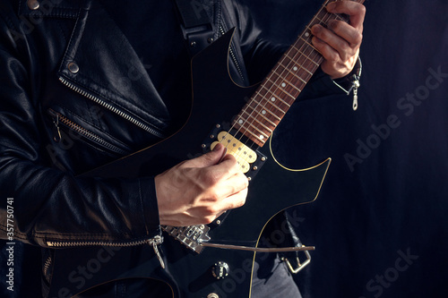 A man wearing a leather jacket playing a black and yellow electric guitar with black background. Rock and music concept