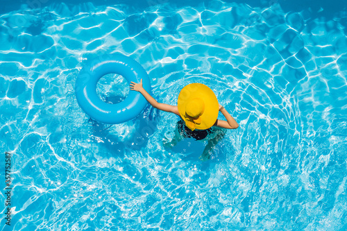 Obraz na plátně Woman sitting in a swimming pool on a ring pool float in a large yellow sunhat