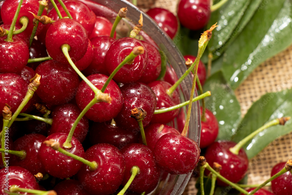 red cherries in a transparent glass bowl on a wooden background, with green leaves of a cherry tree. Summer berries. Yummy. red cherries in a transparent glass bowl on a wooden background, with green leaves of a cherry tree. Summer berries. Yummy.