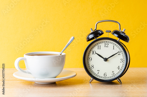 white tea Cup and alarm clock on yellow background
