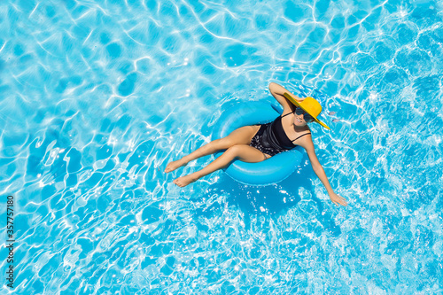 Woman sitting in a swimming pool on a ring pool float in a large yellow sunhat