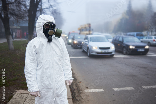 Close up of scientist looking at road with cars, waiting for green light. Selective focus of man in gas mask and protective costume posing near pedestrian crossing. Environmental disaster, fog. © anatoliy_gleb