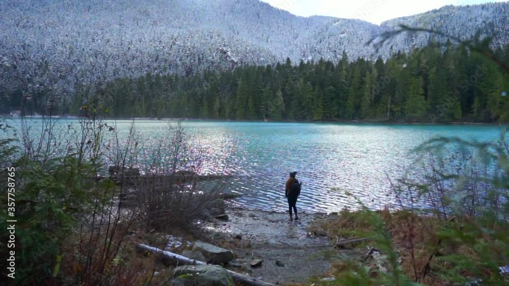 Slow motion panning shot of woman exploring lake in forest during winter - Cheakamus Lake, British Columbia Slow motion panning shot of woman exploring lake in forest during winter - Cheakamus Lake, British Columbia