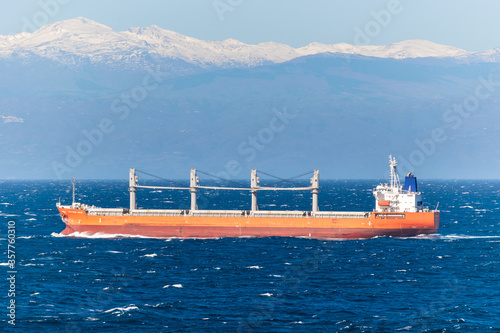 Cargo Bulk Carrier vessel, sailing across the Atlantic Ocean with coast mountains of Spain in the background