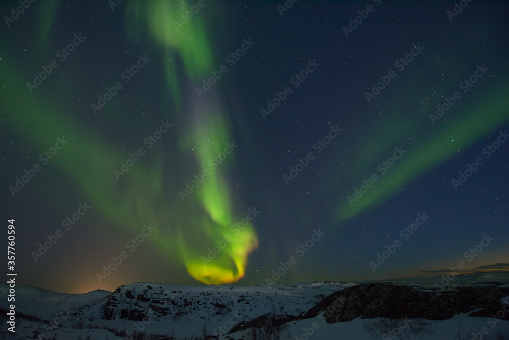 Northern lights over tundra and rocks.