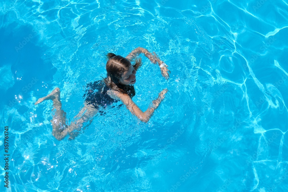 Fototapeta premium Kid has fun in an outdoor pool, child girl swims, dives, plays on the water, blue background