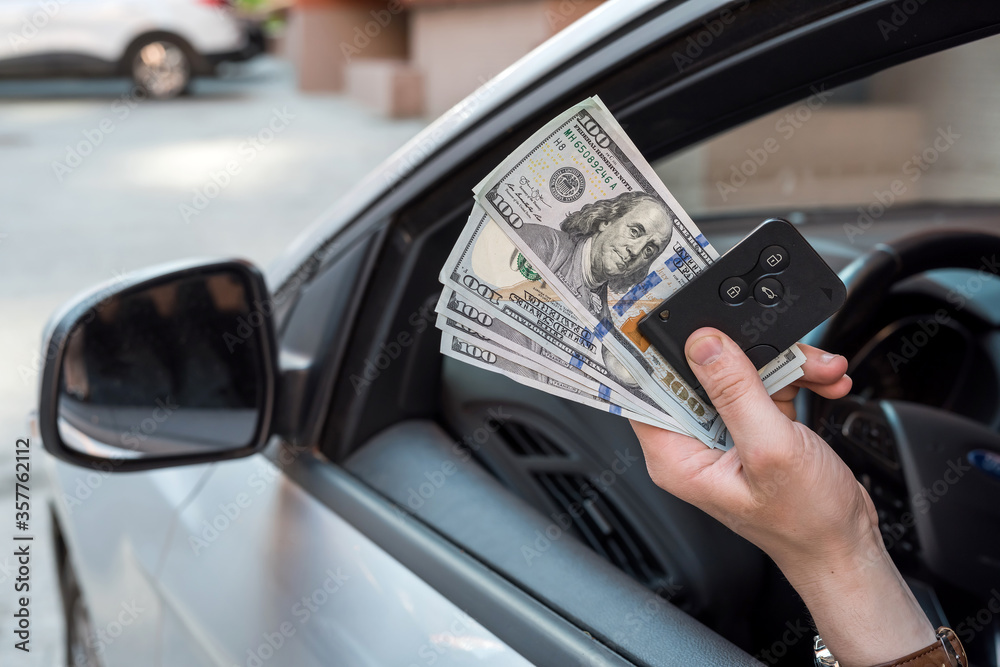 male's hand sitting in car holding dollar and car key
