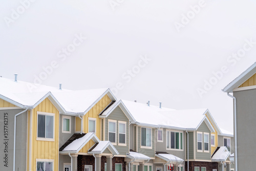 Facade of townhomes with snow covered pitched and valley roof against cloudy sky