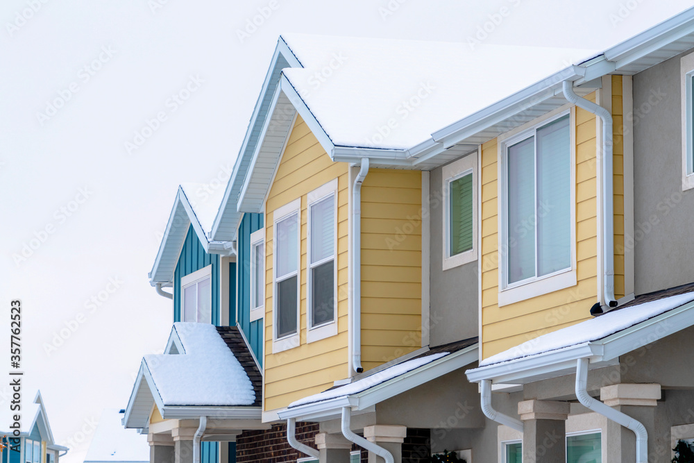 Townhome exterior with snowy gable valley roof against overcast sky in winter Townhome exterior with snowy gable valley roof against overcast sky in winter