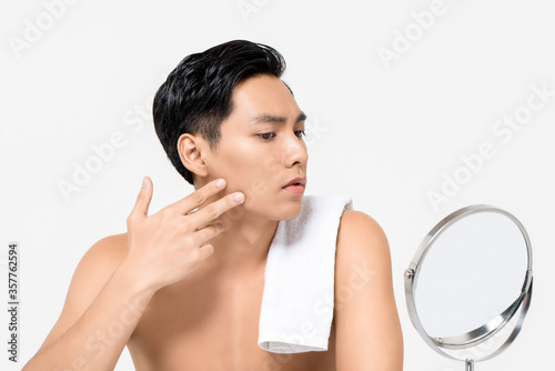 Shirtless young handsome Asian man looking at his face in the mirror  isolated on white background for skin care and beauty concepts