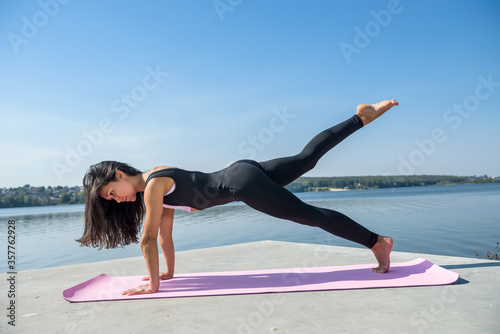 young female athlete doing push-ups outdoors near the lake at daytime. Healthy lifestyle.