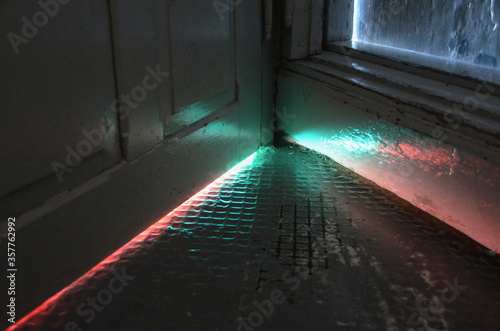 Quadro em tela Light in strange colors seen coming from under a door.