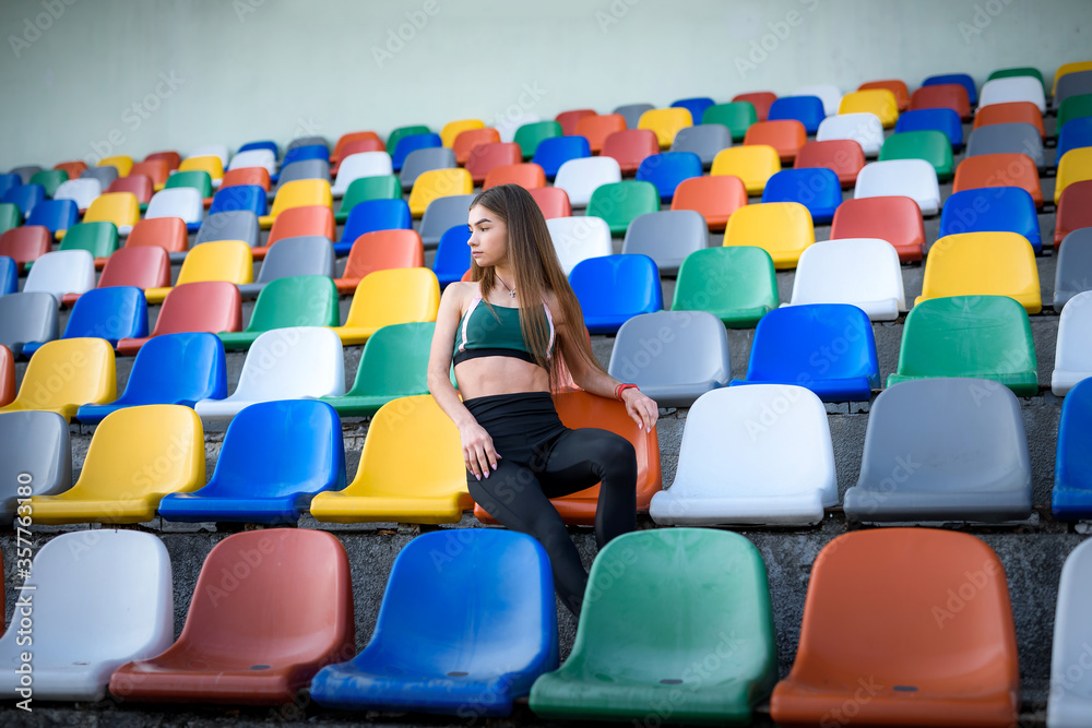 Naklejka premium Portrait of a young sports woman on the stairs after morning jogging in the city stadium. Healthy lifestyle in the city.