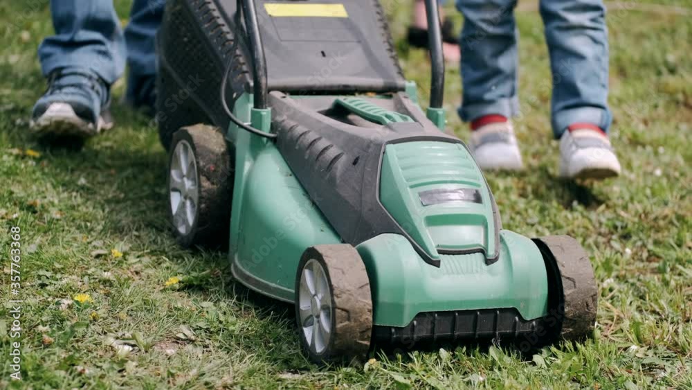 Parents and kids plant tree. Adults teach kids gardening. Person uses machine for cutting grass. Parents and kids plant tree. Adults teach kids gardening. Person uses machine for cutting grass.