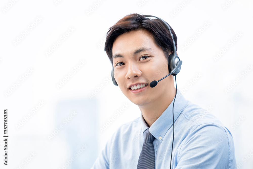 Friendly smiling Asian male telemarketing operator wearing microphone headsets ready to service Friendly smiling Asian male telemarketing operator wearing microphone headsets ready to service