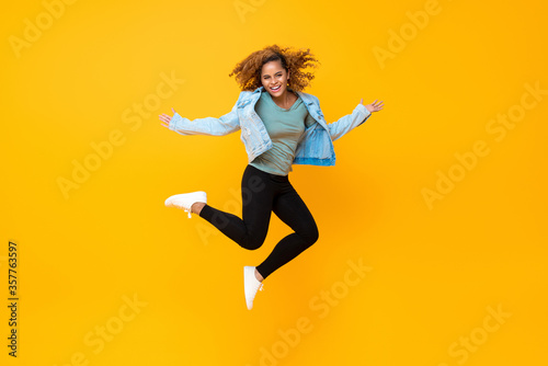 Happy energetic smiling young African-American woman jumping isolated on yellow background