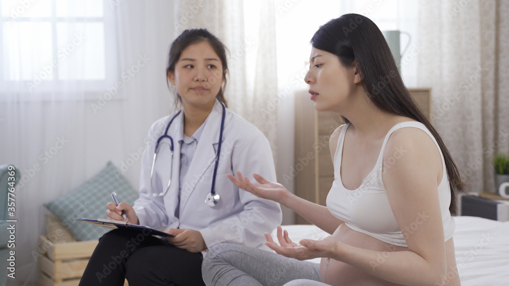 Fototapeta premium japanese lady having antenatal depression is complaining to psychiatrist during home visit. female consultant listening attentively to her case. pregnancy and mental health