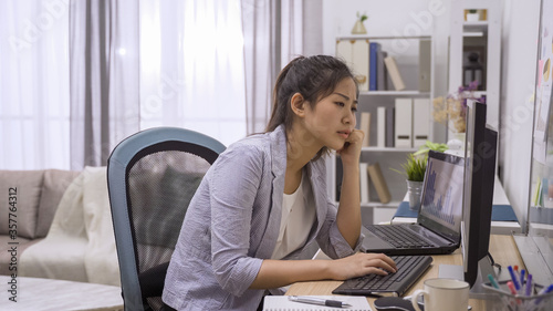 side view portrait of businesswoman sitting at home office desk and thinking solution while working on computer in cozy workplace. thoughtful beautiful lady employee leaning on desk with hand on chin