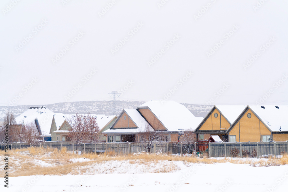 Homes with snowy pitched roofs against hill and cloudy sky on a cold winter day Homes with snowy pitched roofs against hill and cloudy sky on a cold winter day