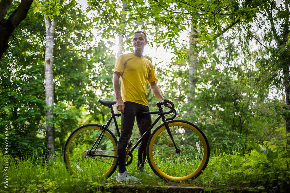 A young Man stopped to rest With his Bicycle in a public Park. He enjoys an early Sunny morning in the forest. A young Man stopped to rest With his Bicycle in a public Park. He enjoys an early Sunny morning in the forest.