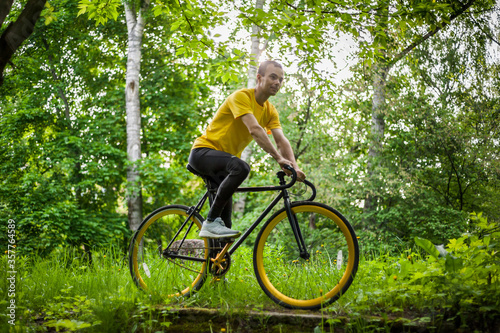 A young Man stopped to rest With his Bicycle in a public Park. He enjoys an early Sunny morning in the forest.