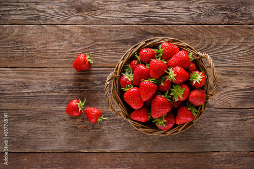 Strawberry in basket with twigs and leaves on rustic wooden table closeup