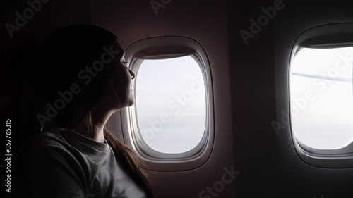 woman in grey t-shirt silhouette against airliner bright windows resting and enjoying in passenger cabin closeup