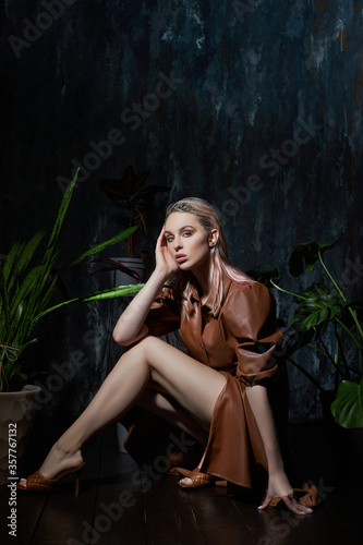 Portrait of a woman in tropical foliage. Wet hair, perfect figure and makeup. Beautiful blonde girl in leather dress and monstera leaves