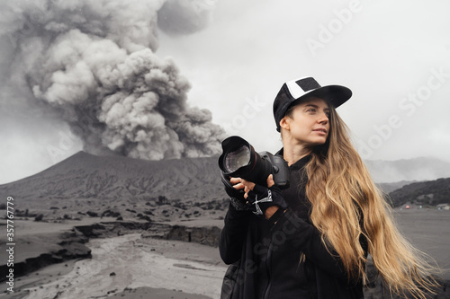 Murais de parede girl travel photographer stands with camera against the backdrop of an erupting volcano