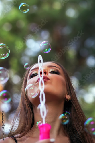 A happy girl blowing soap bubbles in summer park