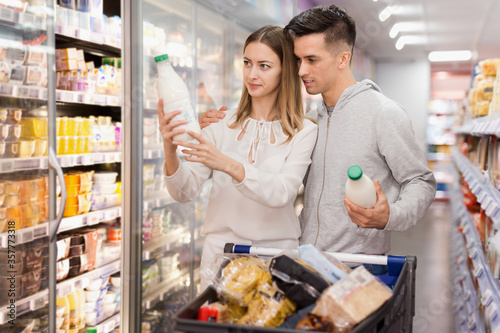 Portrait of young man with girlfriend choosing dairy products in supermarket