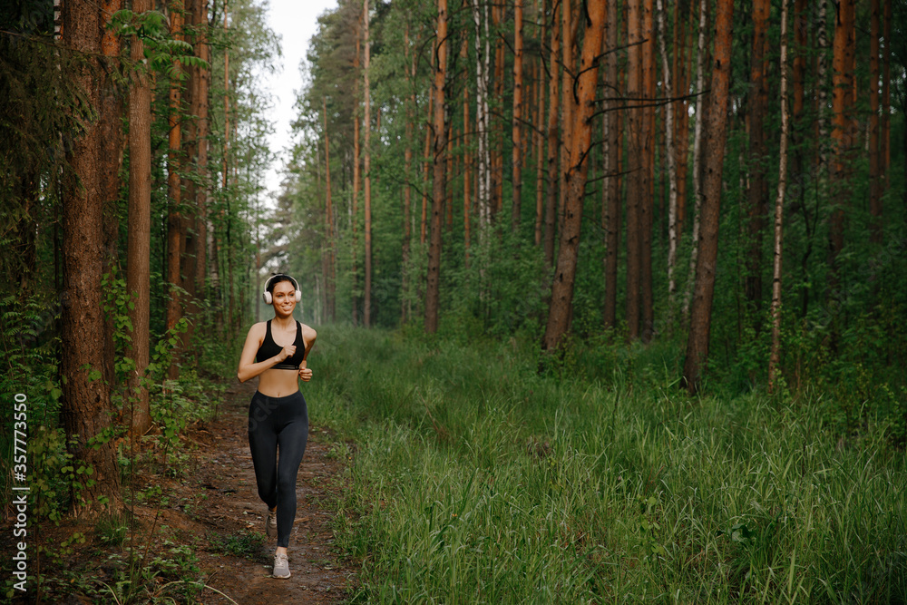 A girl in sports clothes and white Bluetooth headphones runs through the woods A girl in sports clothes and white Bluetooth headphones runs through the woods