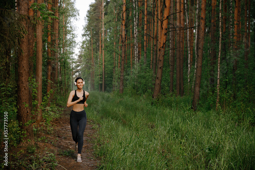 A girl in sports clothes and white Bluetooth headphones runs through the woods