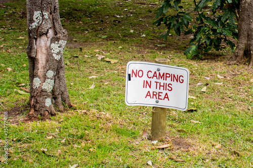 No camping in this area sign on a green grass surrounded by trees.