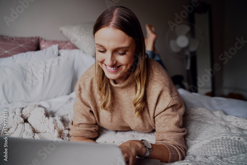 Portrait of cheerful young businesswoman working on her laptop in her bedroom at home - student learning online courses a