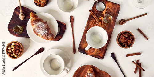 pattern, composition of coffee cups and croissants, nuts, honey and wooden spoons, top view on a white background