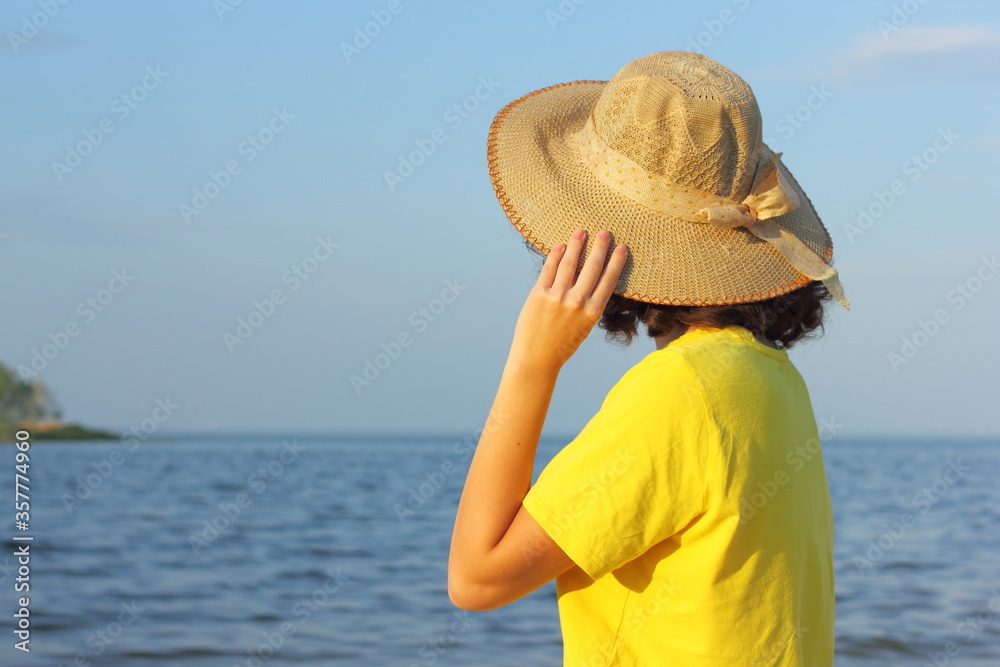 Young girl in a hat looks at the sea