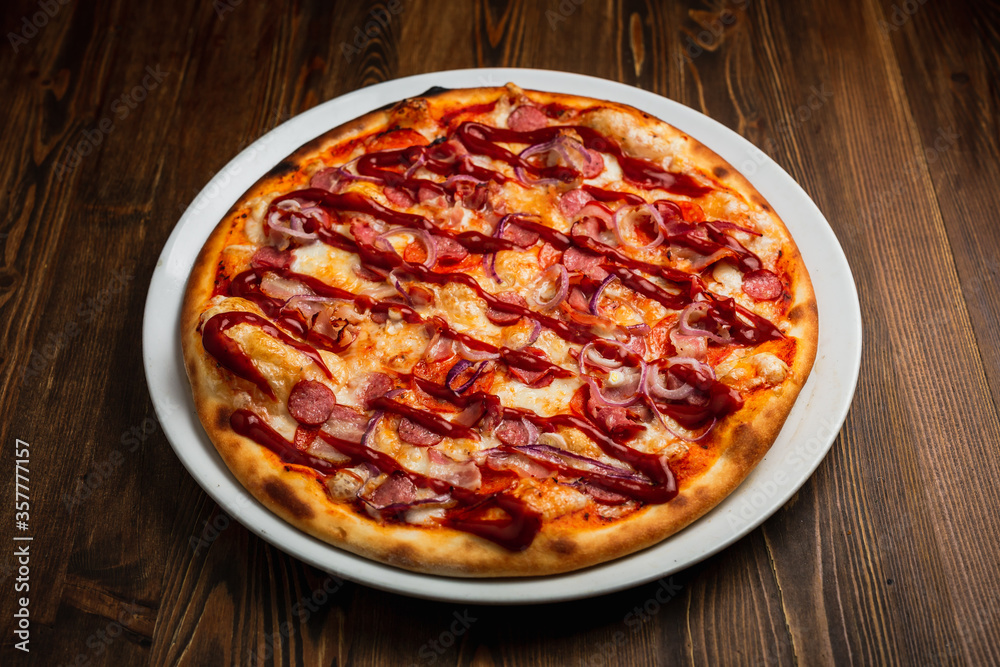 Pepperoni, bacon, sausage, onion and barbeque sauce pizza, wooden background, low key