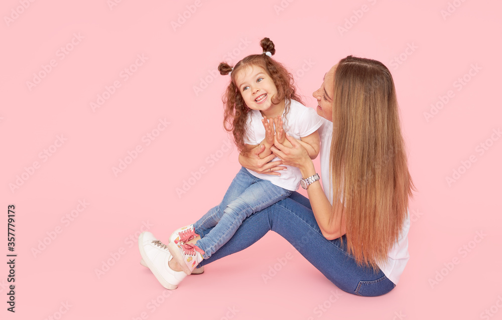 Family values. Mom and daughter in white t-shirts and jeans play and hug on a pink background. Caring for loved ones. Happy motherhood Family values. Mom and daughter in white t-shirts and jeans play and hug on a pink background. Caring for loved ones. Happy motherhood